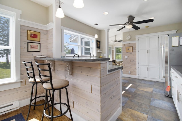 2177 S Lakeshore Dr, Ludington, MI 49431 - kitchen featuring freestanding refrigerator, a ceiling fan, a kitchen bar, a baseboard radiator, and white cabinetry