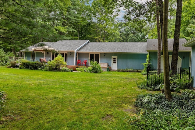 ranch-style home with a front yard, roof with shingles, and view of wooded area