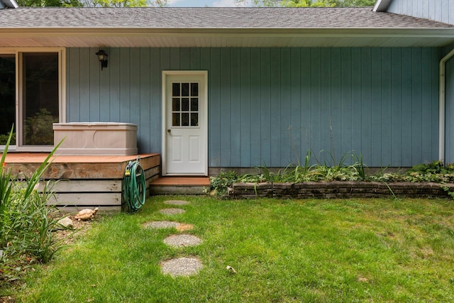 doorway to property with a shingled roof and a lawn