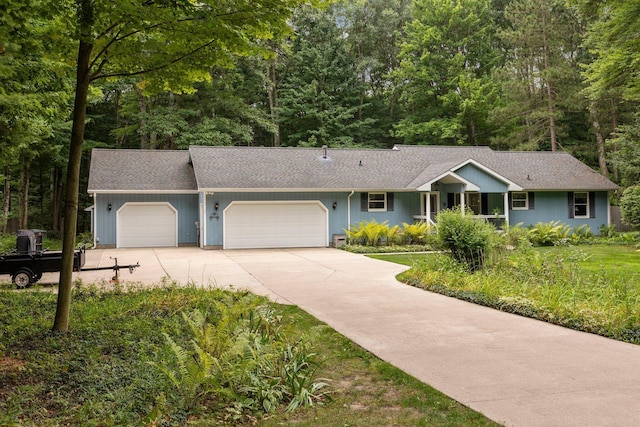 ranch-style home with an attached garage, driveway, a shingled roof, and a forest view