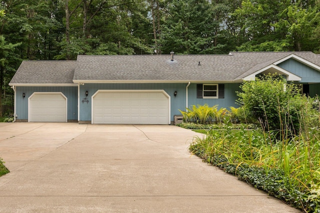 ranch-style house featuring an attached garage, concrete driveway, a shingled roof, and view of scattered trees