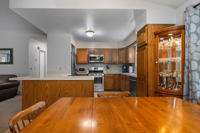 kitchen with appliances with stainless steel finishes, brown cabinets, vaulted ceiling, and a peninsula