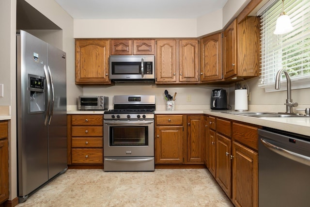 kitchen featuring stainless steel appliances, a sink, brown cabinetry, and light countertops