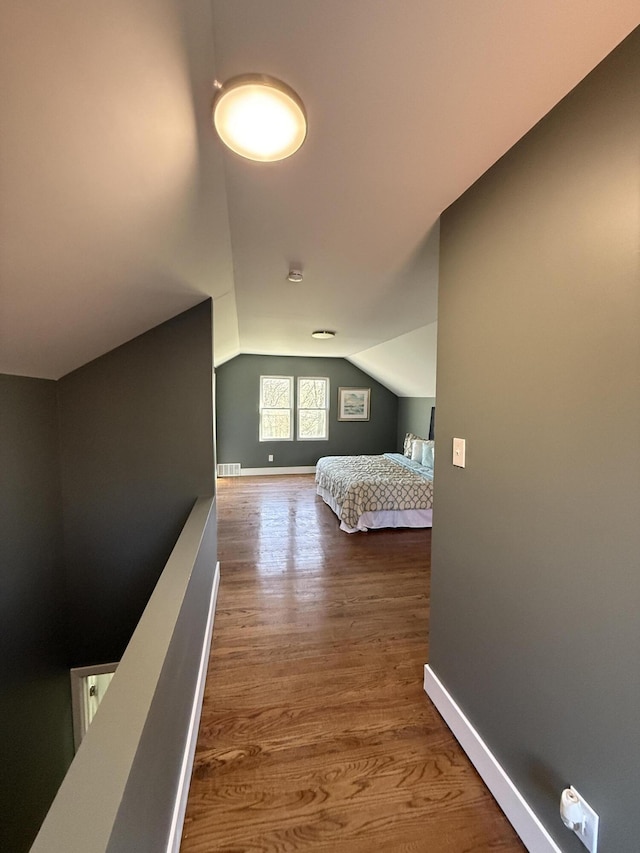 bedroom with vaulted ceiling, wood finished floors, and baseboards