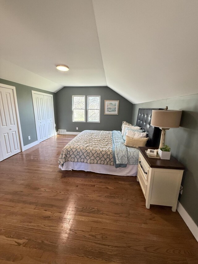bedroom featuring vaulted ceiling, dark wood finished floors, multiple closets, and baseboards