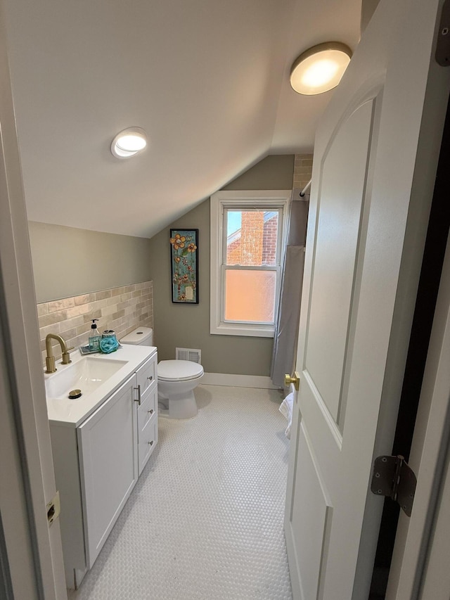 bathroom with vaulted ceiling, vanity, toilet, backsplash, and a shower