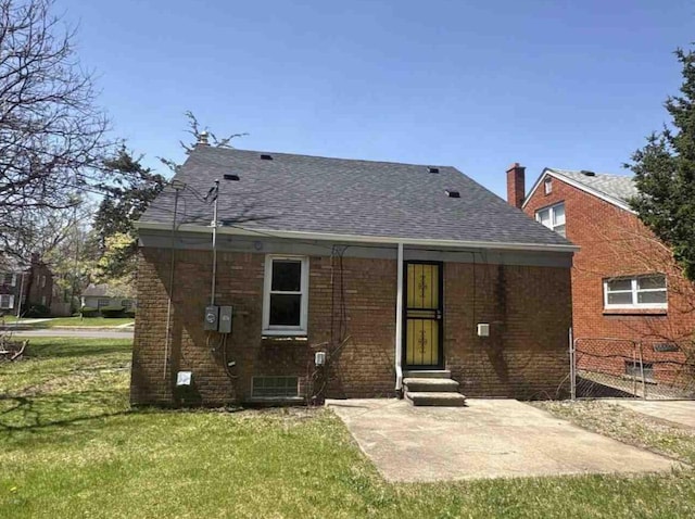 rear view of house with entry steps, a yard, roof with shingles, and brick siding