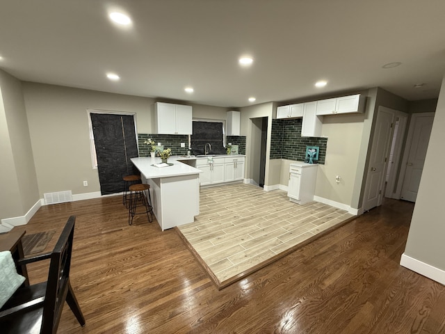 kitchen with a peninsula, tasteful backsplash, light wood-type flooring, a kitchen breakfast bar, and recessed lighting