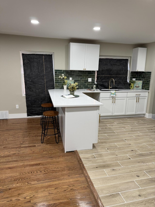 kitchen featuring a sink, light wood-style flooring, decorative backsplash, white cabinets, and recessed lighting