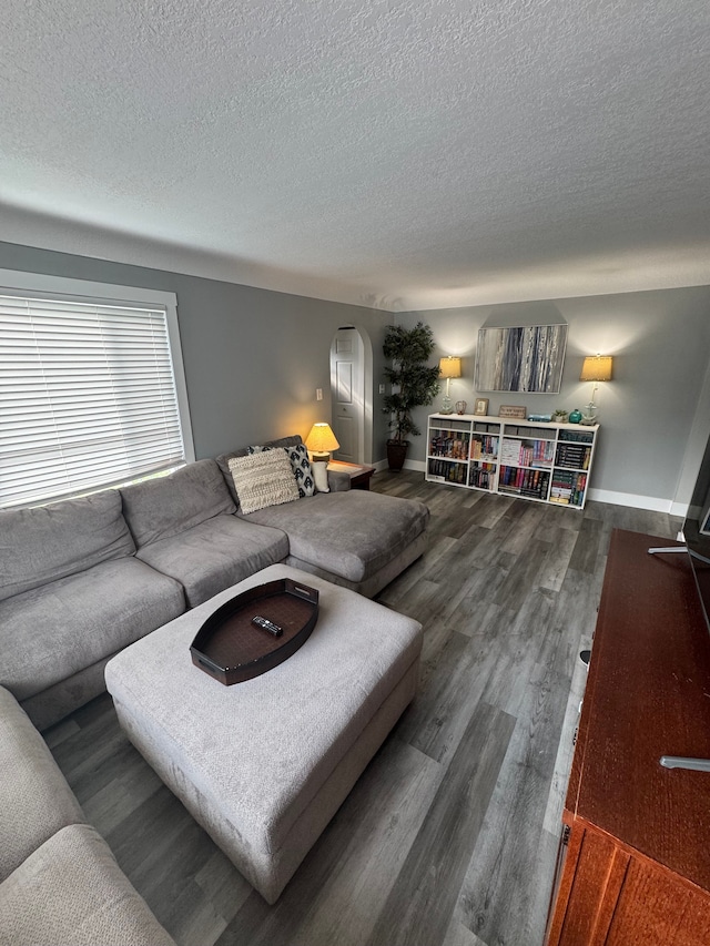 living area featuring arched walkways, dark wood finished floors, a textured ceiling, and baseboards