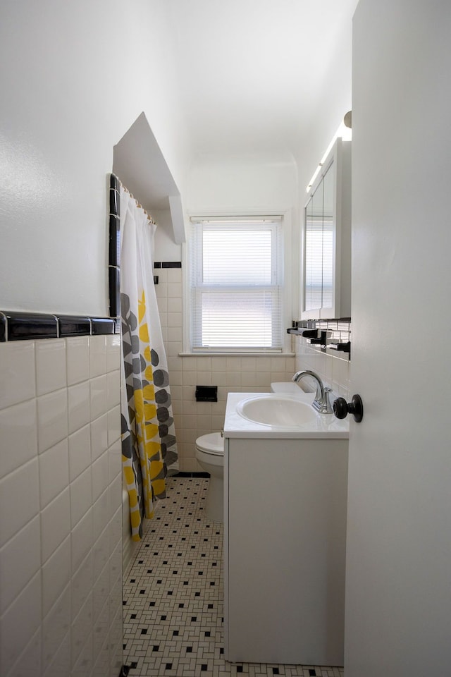full bath with tile walls, toilet, vanity, a shower with shower curtain, and a wainscoted wall