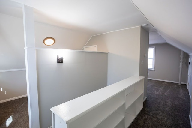 hall featuring dark colored carpet, vaulted ceiling, baseboards, and an upstairs landing