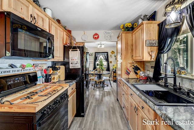 kitchen with black appliances, a sink, light wood-style flooring, tasteful backsplash, and dark countertops