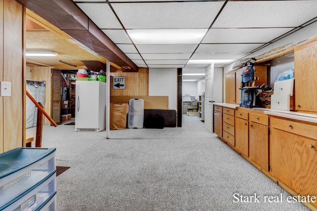 finished below grade area featuring freestanding refrigerator, light colored carpet, and a drop ceiling
