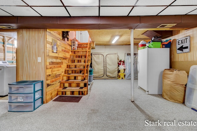 below grade area with washer / clothes dryer, carpet flooring, wood walls, freestanding refrigerator, and a drop ceiling