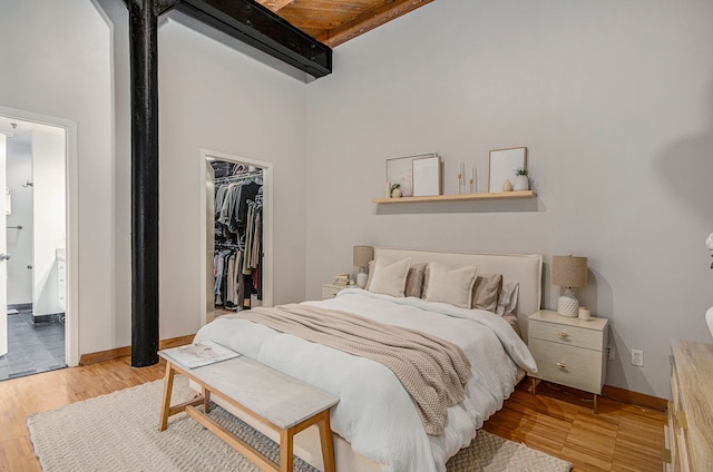 bedroom with a spacious closet, high vaulted ceiling, beamed ceiling, light wood-type flooring, and a closet