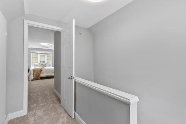 hall featuring carpet, baseboards, and an upstairs landing