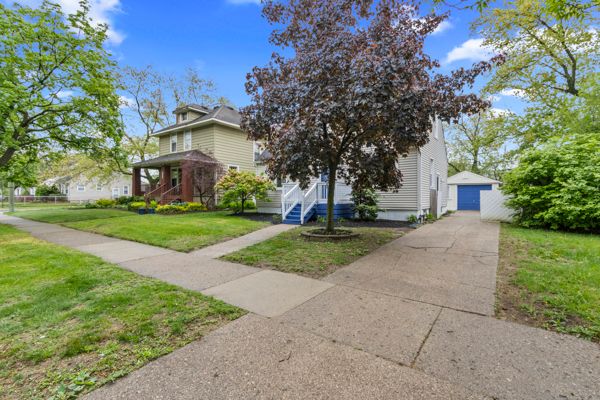american foursquare style home with a detached garage, concrete driveway, a front yard, and an outbuilding