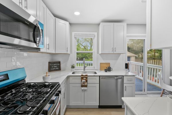 kitchen featuring stainless steel appliances, a sink, light stone counters, backsplash, and light wood-type flooring