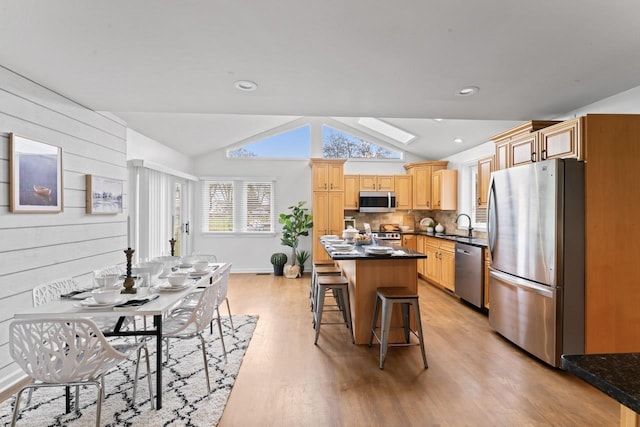 12147 Torrey Rd, Fenton, MI 48430 - kitchen featuring stainless steel appliances, vaulted ceiling, light wood-style floors, a kitchen bar, and dark countertops