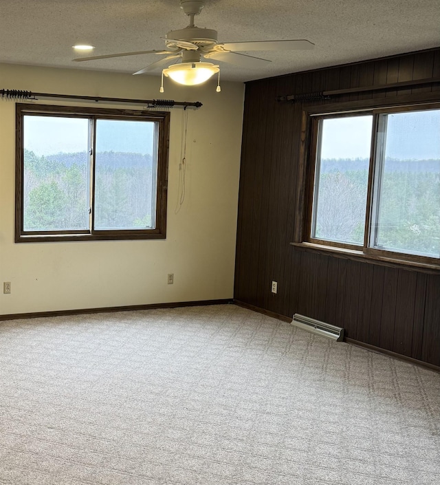 3135 Montgomery Rd, Bellaire, MI 49615 - carpeted empty room featuring wooden walls, ceiling fan, baseboards, a textured ceiling, and a baseboard radiator