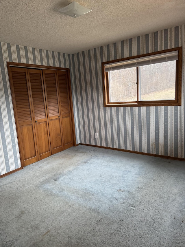 3135 Montgomery Rd, Bellaire, MI 49615 - unfurnished bedroom featuring wallpapered walls, carpet flooring, a closet, a textured ceiling, and baseboards