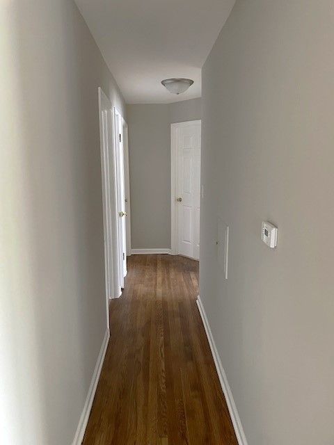 corridor featuring dark wood-type flooring and baseboards
