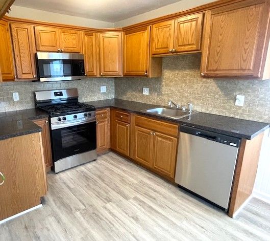 kitchen featuring appliances with stainless steel finishes, a sink, brown cabinetry, light wood-style flooring, and dark countertops