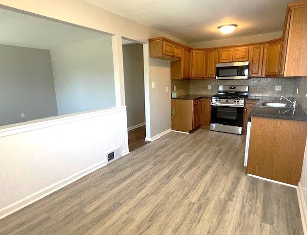 kitchen featuring stainless steel appliances, a sink, brown cabinetry, light wood finished floors, and decorative backsplash
