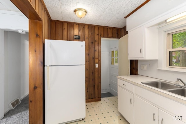 1001 Kelsey Ave, Lansing, MI 48910 - kitchen featuring freestanding refrigerator, a sink, wooden walls, white cabinets, and light flooring