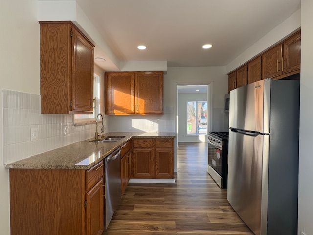 kitchen featuring appliances with stainless steel finishes, a sink, wood finished floors, brown cabinets, and recessed lighting