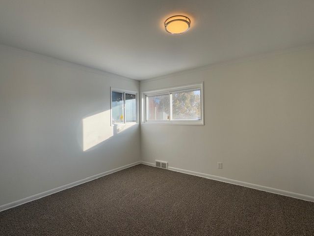 empty room featuring dark carpet, ornamental molding, and baseboards