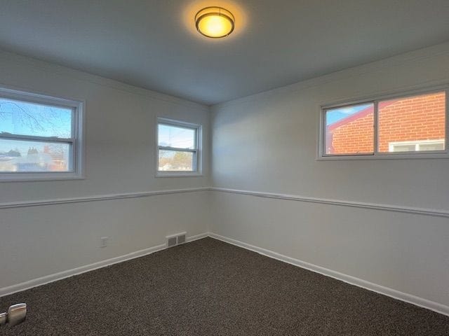 unfurnished room with dark colored carpet, plenty of natural light, and baseboards