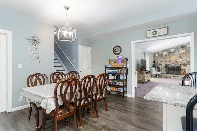 dining area featuring stairs, dark wood finished floors, a chandelier, a stone fireplace, and baseboards