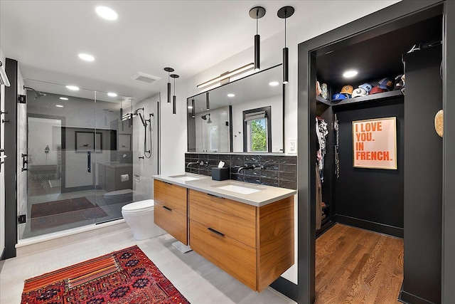bathroom with a stall shower, toilet, double vanity, tasteful backsplash, and recessed lighting