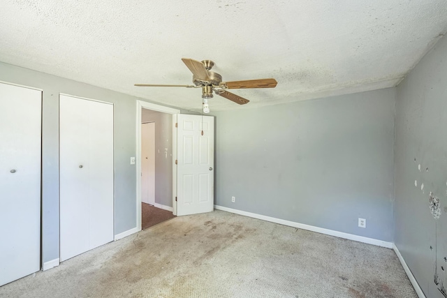 unfurnished bedroom featuring carpet floors, baseboards, a textured ceiling, ceiling fan, and multiple closets