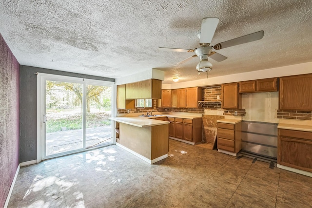 kitchen featuring a peninsula, brown cabinetry, ceiling fan, a sink, and baseboards