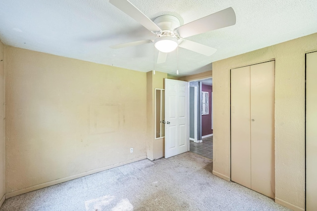 unfurnished bedroom with carpet flooring, baseboards, ceiling fan, a textured ceiling, and two closets