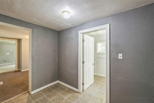 hall with a textured wall, a textured ceiling, and baseboards