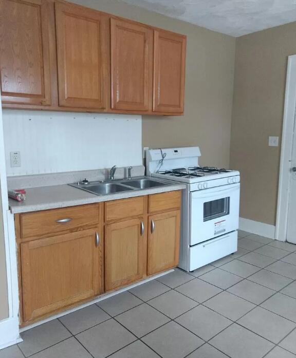 39 Iona Ave, Muskegon, MI 49442 - kitchen with white gas stove, a sink, light countertops, light tile patterned floors, and baseboards