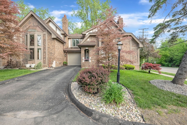 652 S Military St, Dearborn, MI 48124 - tudor house featuring a chimney, a garage, driveway, brick siding, and a front yard