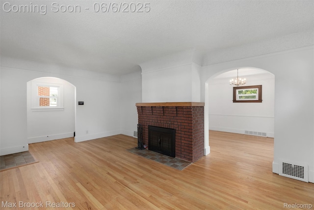 1215 Irving Ave, Royal Oak, MI 48067 - unfurnished living room with arched walkways, a fireplace, wood finished floors, a chandelier, and a textured ceiling