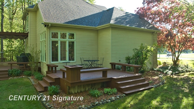 back of house featuring a shingled roof, a wooden deck, and a lawn
