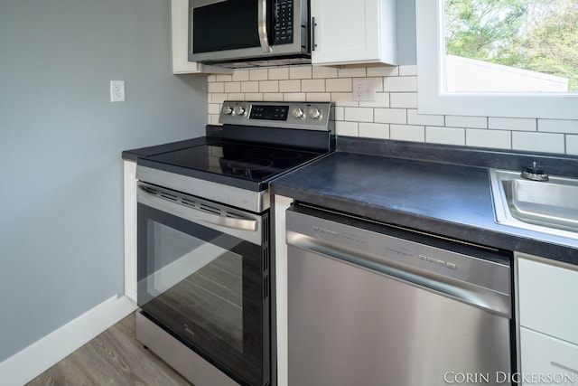 3188 E Stage Rd, Ionia, MI 48846 - kitchen with appliances with stainless steel finishes, dark countertops, white cabinets, backsplash, and wood finished floors