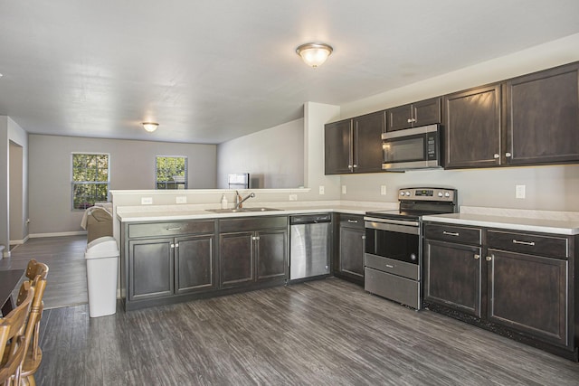 kitchen with appliances with stainless steel finishes, light countertops, a peninsula, dark wood finished floors, and dark brown cabinetry