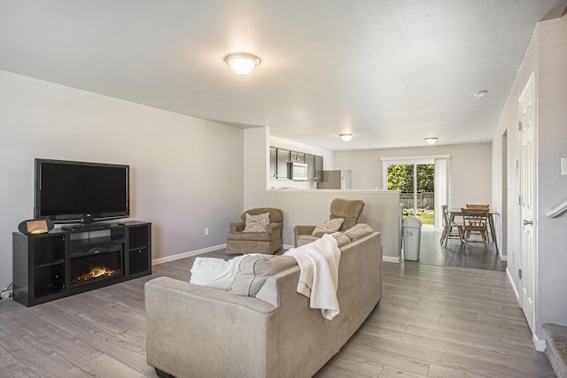 living area featuring wood finished floors, baseboards, and a warm lit fireplace