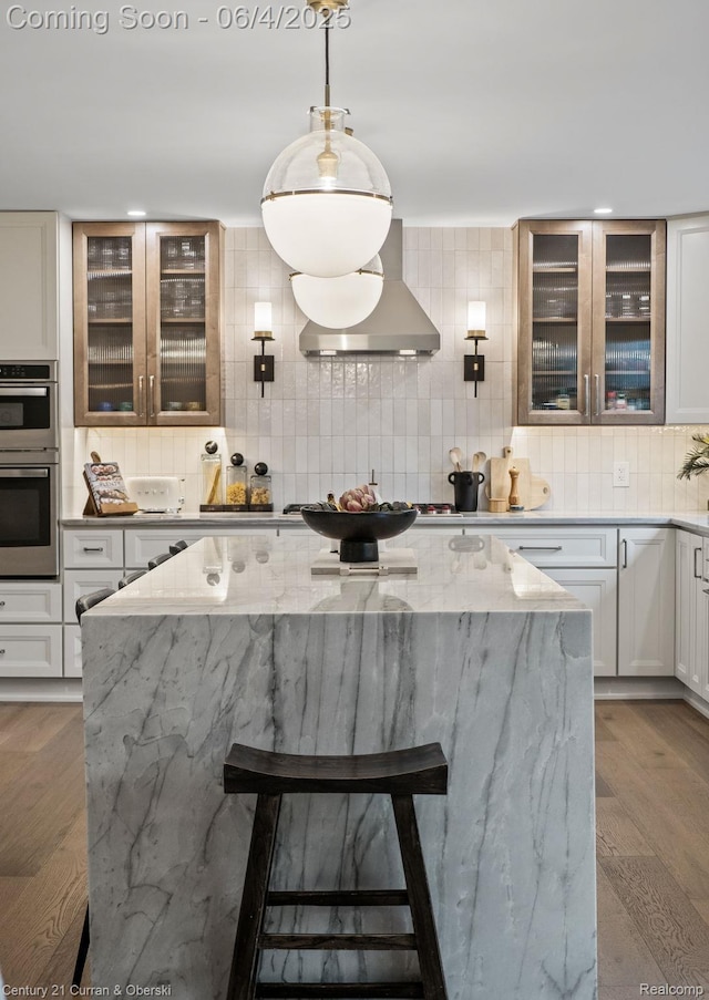 1985 Lone Pine Rd, Bloomfield Hills, MI 48302 - kitchen featuring stainless steel double oven, wall chimney exhaust hood, decorative backsplash, a kitchen island, and a breakfast bar area
