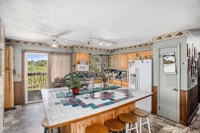 kitchen with tile countertops, white appliances, a textured ceiling, a wainscoted wall, and a ceiling fan