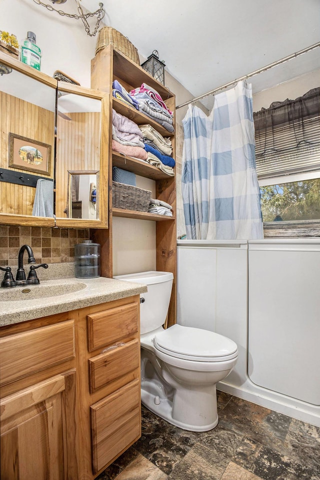 full bath featuring toilet, backsplash, vanity, stone finish floors, and shower / bath combo