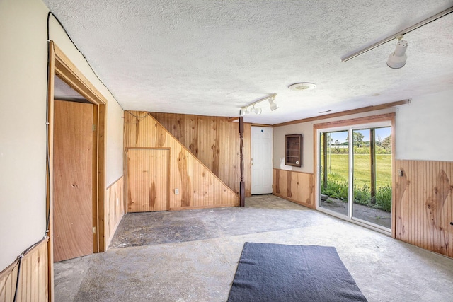 unfurnished room featuring wooden walls, a textured ceiling, rail lighting, and a wainscoted wall